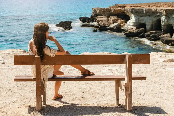 年轻的女人坐在靠近海崖的长椅上 欣赏着海景和自然美 — 图库照片
