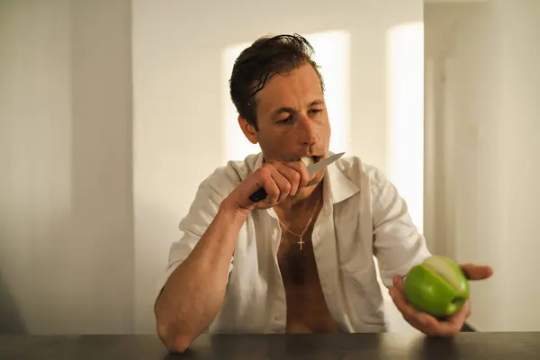 リンゴを切って食べるハンサムな男のシネマティックな肖像画 — ストック写真
