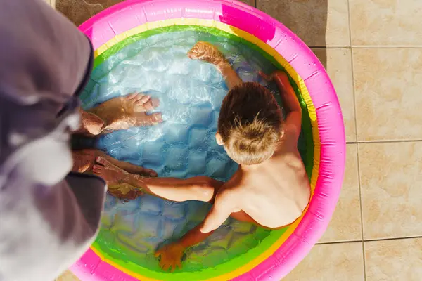 小男孩在父亲脚边的一个充气圆形游泳池里玩耍 — 图库照片