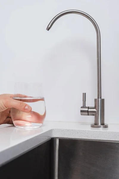 Woman get filtered water from stainless faucet into a glass.