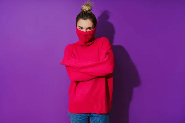 若い女性の肖像画は紫色の背景に対して暖かく居心地の良いポロの首のセーターの内部に彼女の顔を隠しています — ストック写真