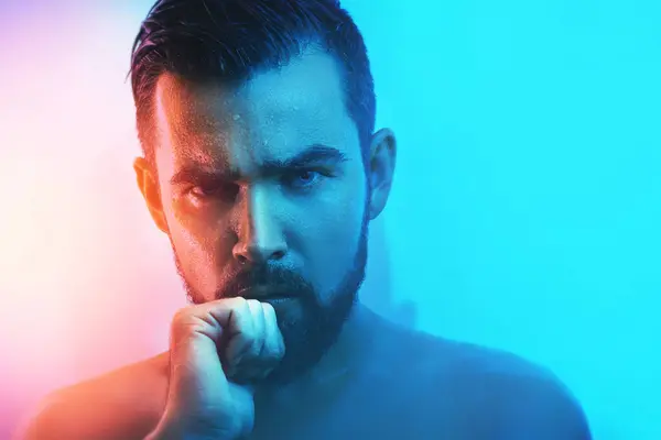 Portrait of handsome young man with wet face in blue and orange light
