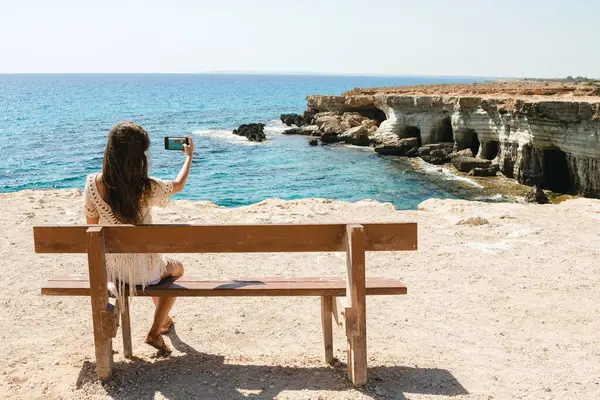 年轻女子在手机上拍了一张照片 照片上是希腊角海崖附近美丽的大海和洞穴 — 图库照片