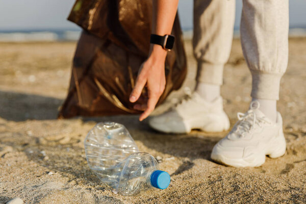 Woman volunteer is collecting plastic waste on the beach to contribute to the effort of keeping nature clean. Closeup of hand with plastic bottle.