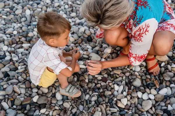 妈妈和她可爱的小儿子在沙滩上捡鹅卵石 — 图库照片