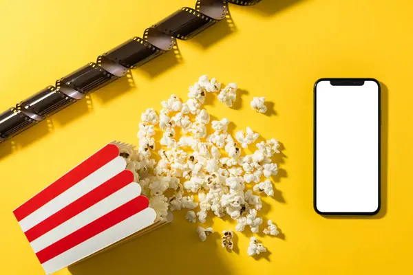 Classic popcorn bucket and smartphone with blank screen on yellow background.