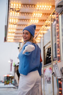 Sıcak kıyafetler giymiş neşeli ve şık bir kadın, karlı bir kış eğlence parkında eğleniyor..