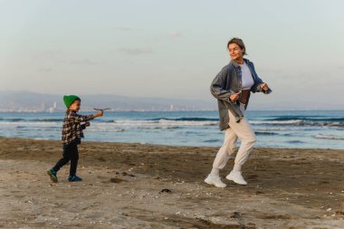 Genç anne ve küçük oğlu gün batımında plajda kovalamaca oynuyorlar..