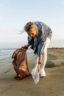 Mutlu kadın gönüllü, doğayı temiz tutma çabalarına katkıda bulunmak için plajda plastik atıkları topluyor..