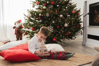 Şirin küçük çocuk, Noel ağacı ve şenlikli süslemelerle süslenmiş sıcak bir oturma odasında şöminenin yanında oynuyor..