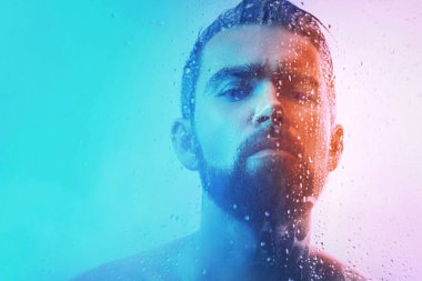 Mavi ve turuncu ışıkta ıslak camdan yakalanan yakışıklı genç adamın portresi..