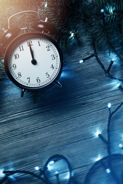 Alarm saati gece yarısına yakın. Etrafı pırıl pırıl Noel ışıkları ve kırsal ahşap bir yüzey üzerinde taze ladin dallarıyla çevrili..