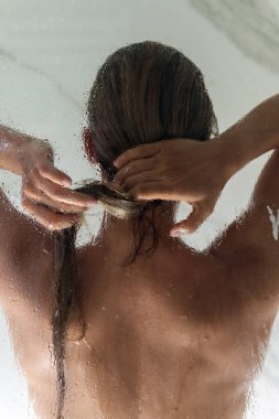 Güzel bir kadın ıslak camın arkasında duş alıyor. Damlacıklara odaklan..