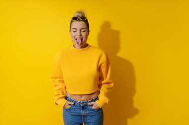 Sarı eşofman altı giyen ve sarı arka planda güneş gözlüğü takan neşeli genç kızın portresi