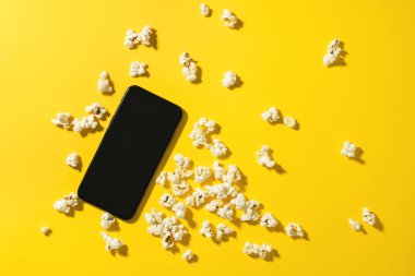 Sarı arka planda boş ekranı olan lezzetli patlamış mısır ve akıllı telefon.