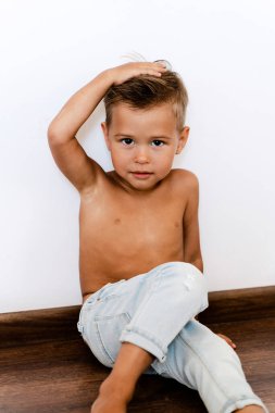 Modeller gibi beyaz duvara poz veren kot pantolon giyen şirin bir çocuk..