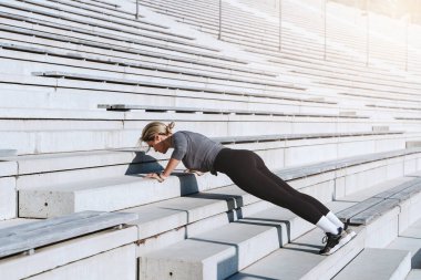 Spor kıyafetleri giyen kadın sporcu spor salonunun merdivenlerinde antrenman yaparken şınav çekiyor.. 