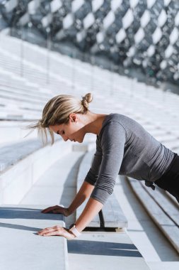 Spor kıyafetleri giyen kadın sporcu spor salonunun merdivenlerinde antrenman yaparken şınav çekiyor.. 