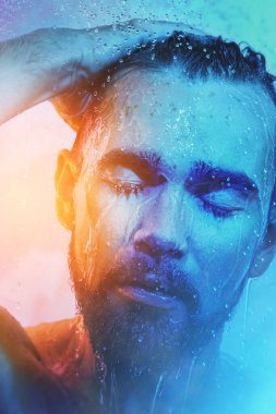 Mavi ve turuncu ışıkta duş altında yakışıklı bir adamın portresi..