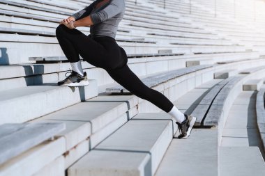 Spor giyinen kadın sporcu açık hava stadyumunun merdivenlerinde bacak esnetiyor..