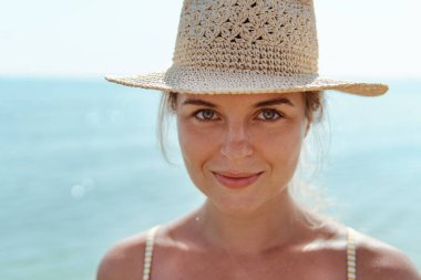 Kadın sarı çizgili bikini ve hasır şapka giyerek yaz havası yayıyor, kumsalda eğleniyor..