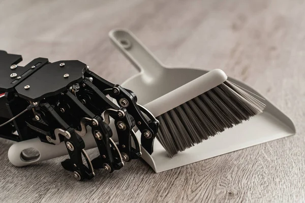 Robotic hand skillfully using a dustpan and brush to sweep the floor.