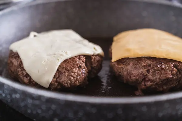 Juicy ground beef hamburger patty in a frying pan, crowned with melting cheese.