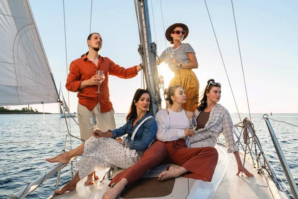 Group of happy friends drinking wine and relaxing on the sailboat during sailing in sea.