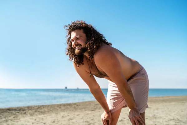 Portrait of cheerful curly man relaxing on the beach during sunny summer day
