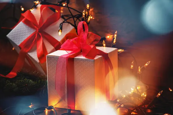 用生机勃勃的红丝带包裹的礼品盒 镶嵌在闪烁的圣诞彩灯和新鲜的云杉枝条之间 — 图库照片