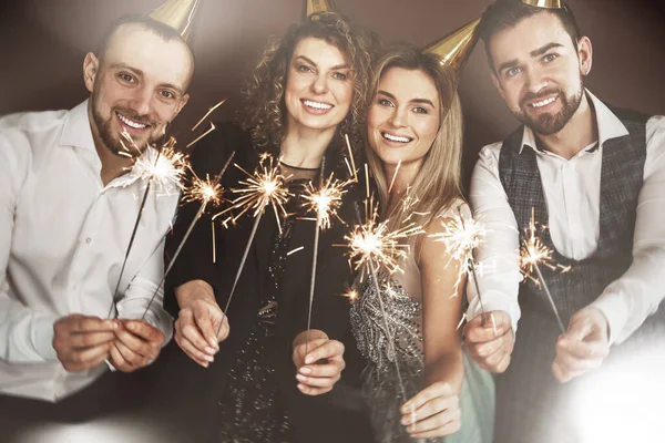 Group of happy people wearing party hats holding burning sparkles during holiday or event celebration