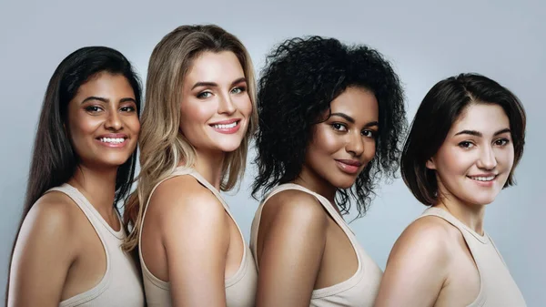 Multi-ethnic beauty and friendship. Group of different ethnicity women smiling and looking at camera on gray background.