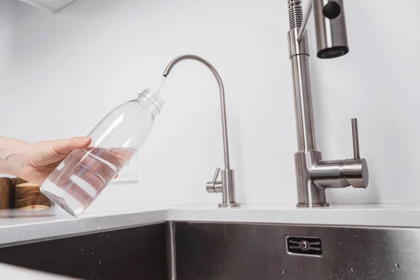 Woman get filtered water from stainless faucet into reusable bottle.