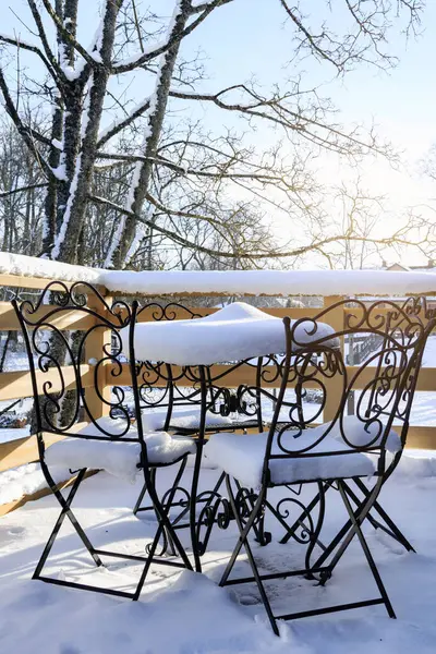 Outdoor table and chairs covered in snow after the first snowfall during sunny day on the baclony