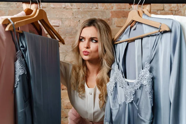 Young beautiful woman and clothing rack with different outfits in store or showroom