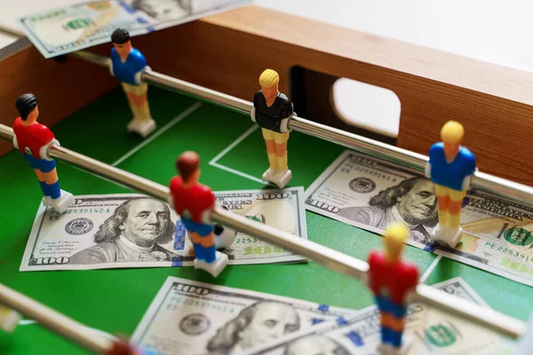 Table football game with US dollar bills scattered around it, alluding to a betting concept and victory