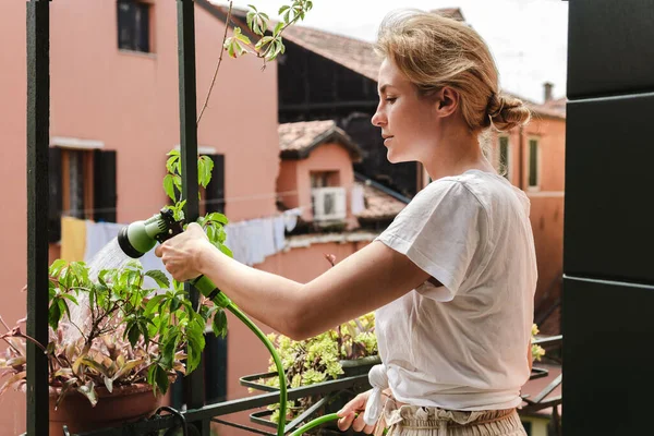 Young woman using watering sprayer to water the plants on tiny balcony