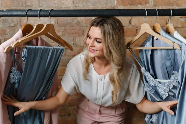 Young beautiful woman and clothing rack with different outfits in store or showroom