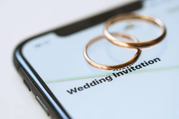 智能手机上的两个金戒指和屏幕上的文字 婚礼邀请函 — 图库照片