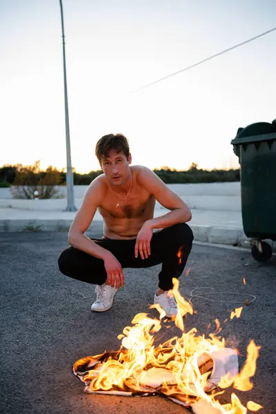Young adult man pyromaniac burning his shirt on the street