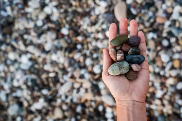 Closeup of female hand with heap of pebbles on shingle beach