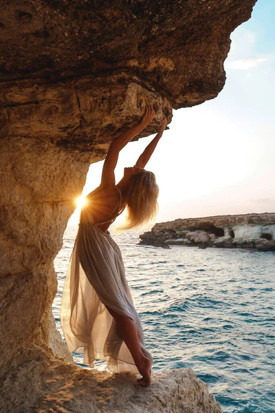日落时穿着飘逸丝裙在悬崖上的女人 — 图库照片