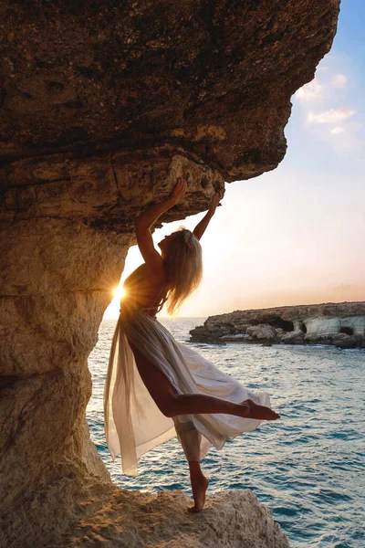 Woman in flowing silk dress on a cliff at sunset.
