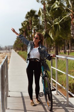 Kot ceketli kadın deniz kenarında bisiklet sürmekten hoşlanıyor..