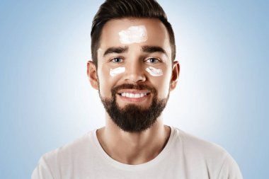 Gülümseyen adam yüzüne yüz kremi sürüyor. Cilt bakımı ve erkekler için kişisel bakım rutinleri.