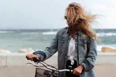 Kot ceketli kadın deniz kenarında bisiklet sürmekten hoşlanıyor..