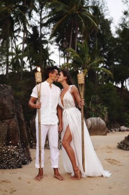 Alacakaranlık plajında meşaleli düğün töreni.