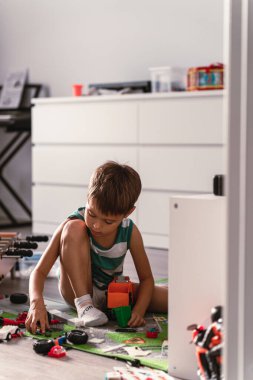 Neşeli çocuk, güneşli modern bir odada oyuncaklarıyla oynuyor..
