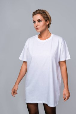 Woman dressed in a white oversized t-shirt with blank space, ideal for a mockup, set against gray background. clipart