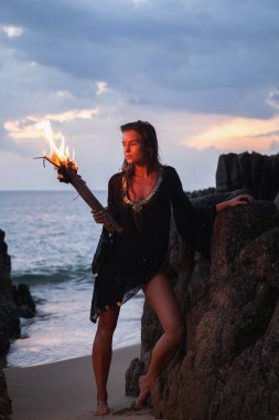 Alacakaranlıkta sahilde elinde yanan bir meşale tutan gizemli bir kadın..